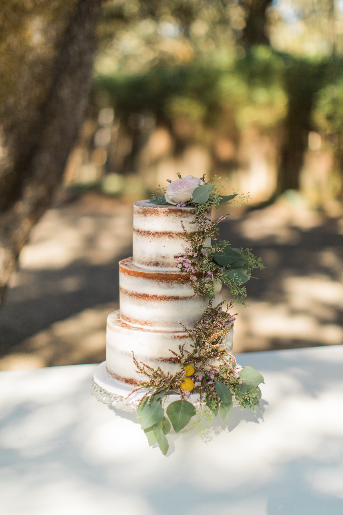 naked wedding cake adorned with greenery and florals