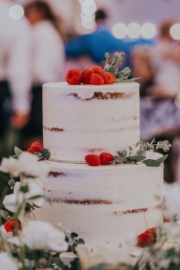 naked wedding cake with rasberries and greenery