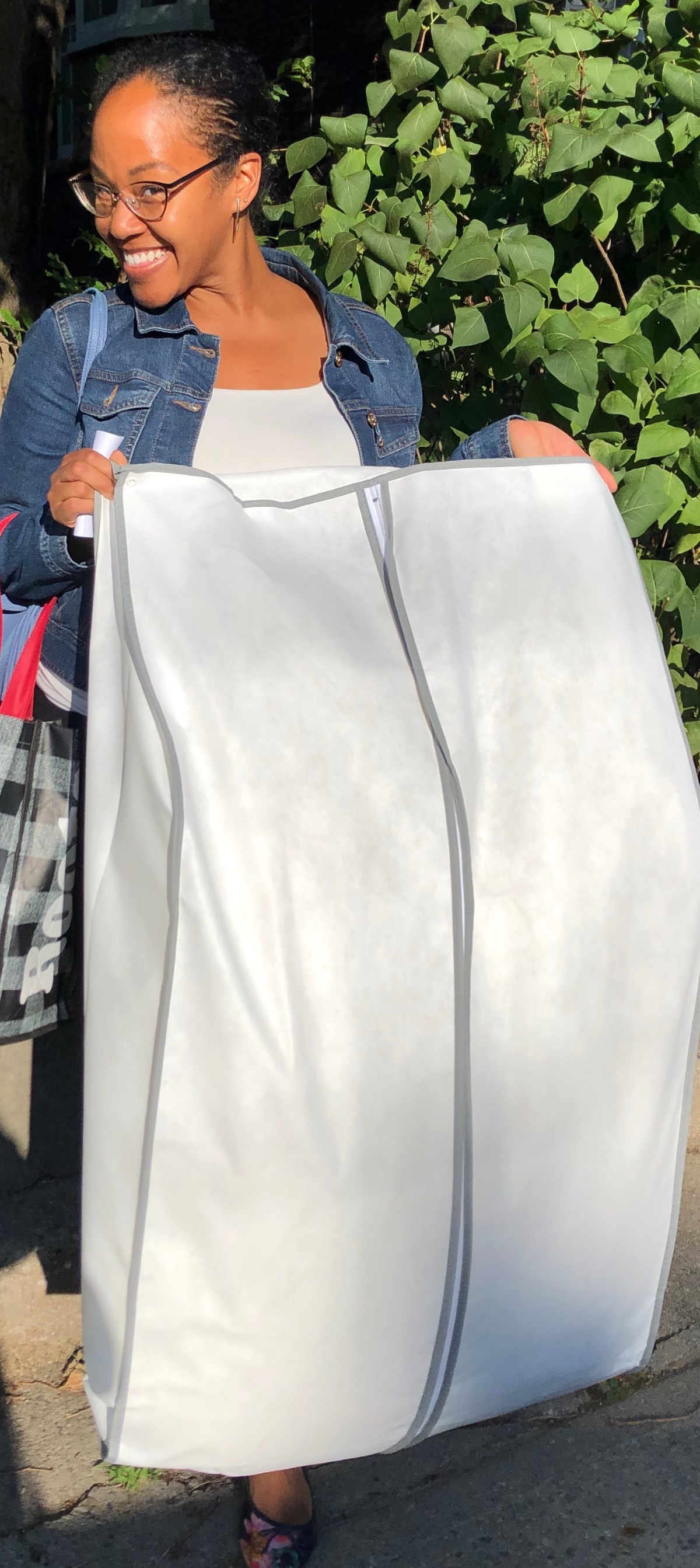 Smiling woman holds up a white garment bag, ready for travel