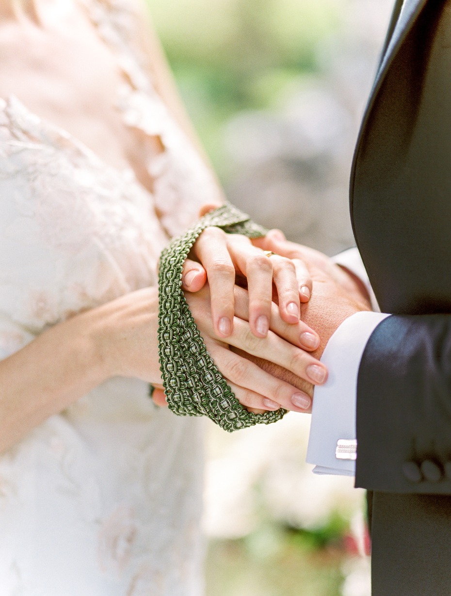 Bride and groom hold hands at wedding, tied together with green ribbon