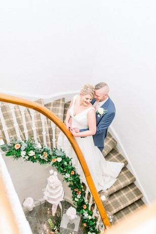 Newlyweds embrace on wedding staircase, cake and flowers