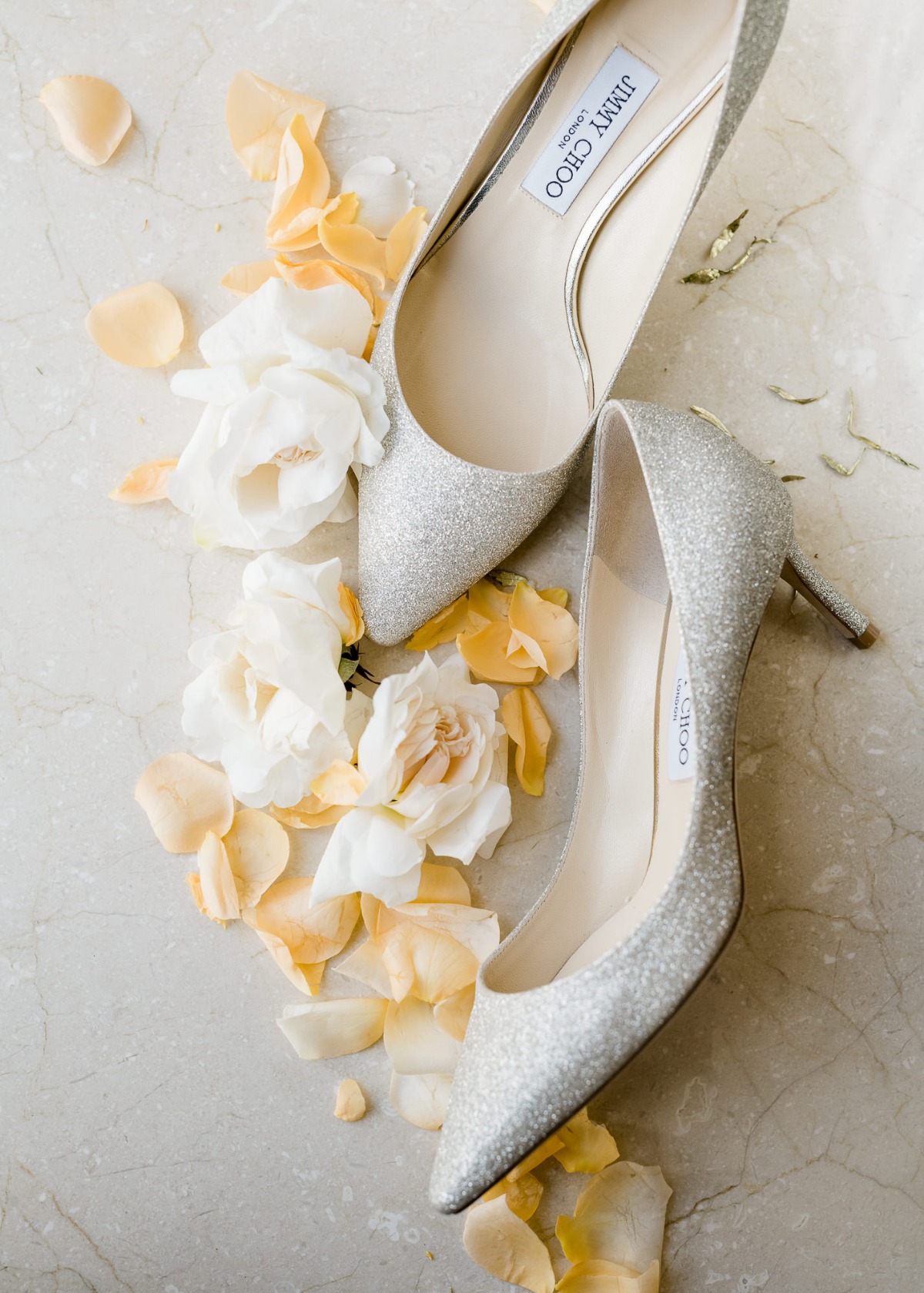 Silver Jimmy Choo wedding shoes with flowers on a marble surface