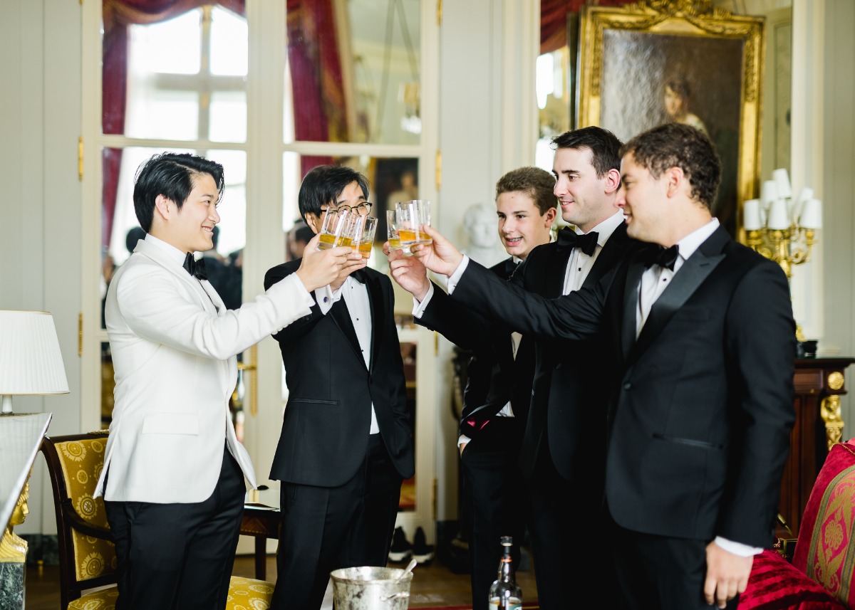 Men in tuxedos cheers with glasses in a luxurious room