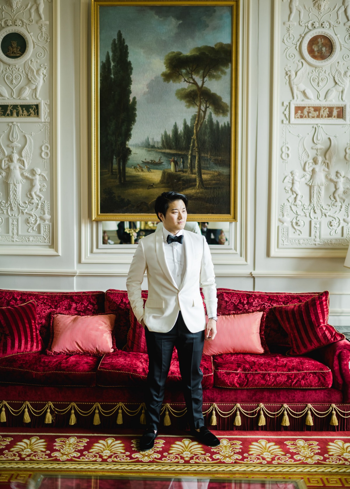 Groom in white suit posing in elegant room with red couch
