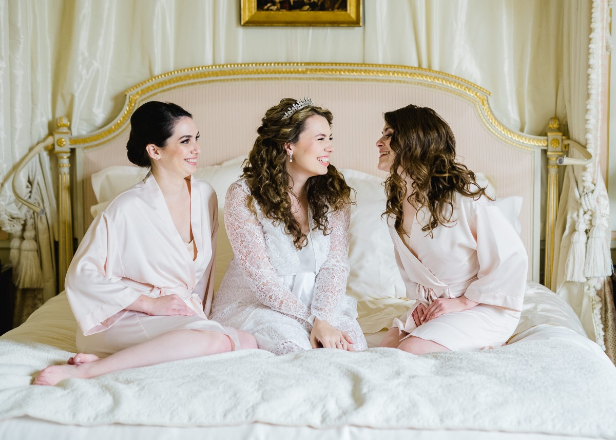Bride and bridesmaids laughing on a bed on a wedding morning