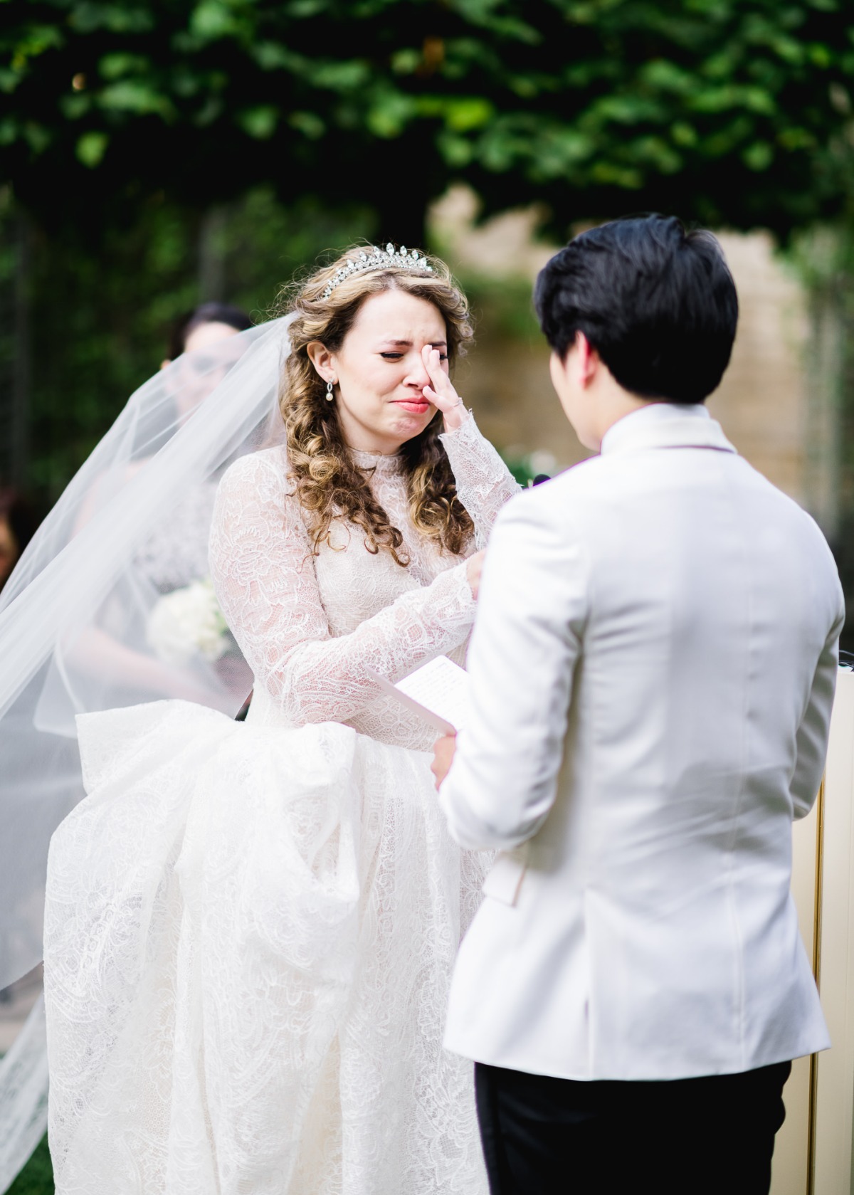 Bride wiping a tear at her wedding ceremony smiling to her groom