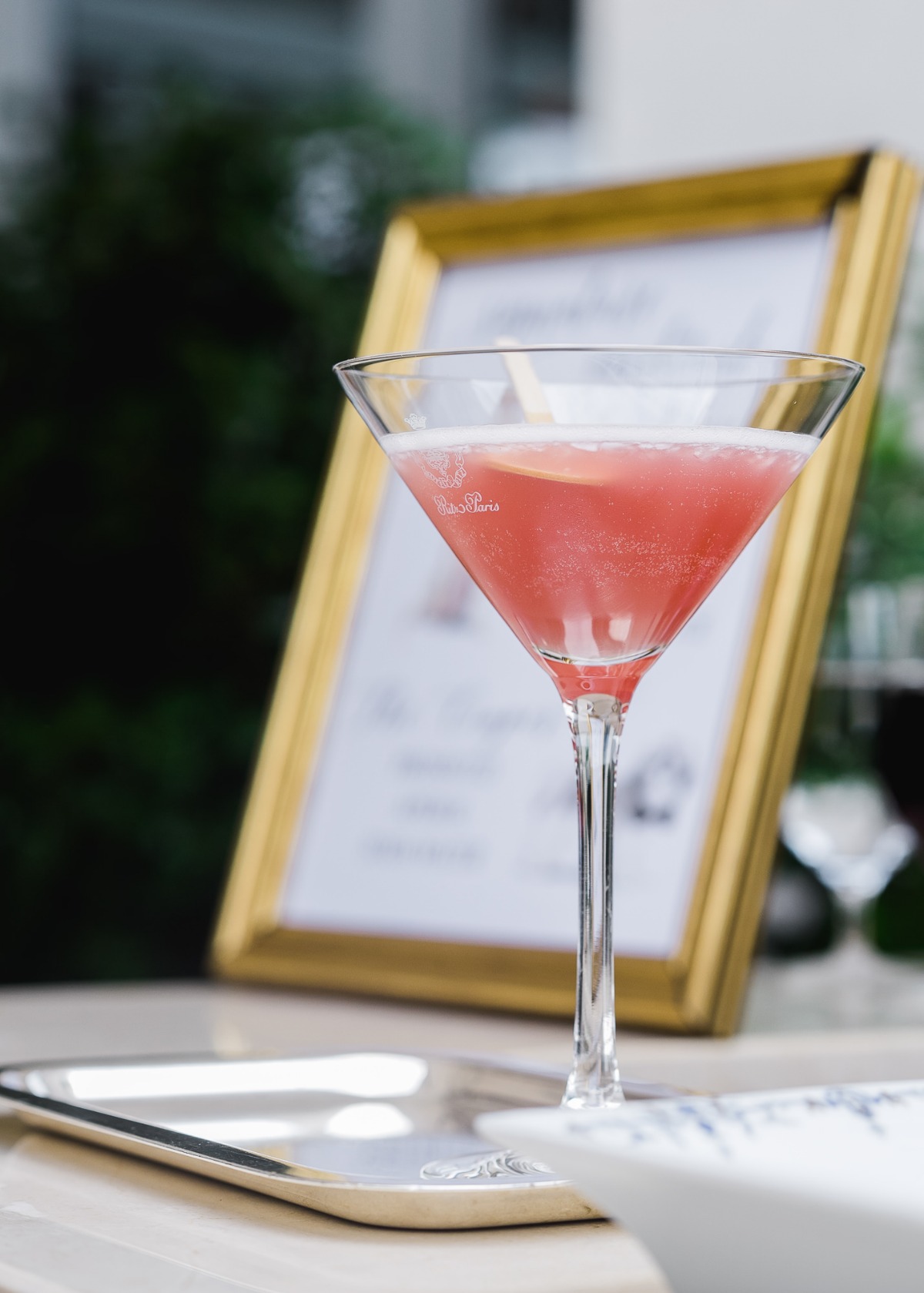 Pink cocktail in a martini glass on a tray with framed art