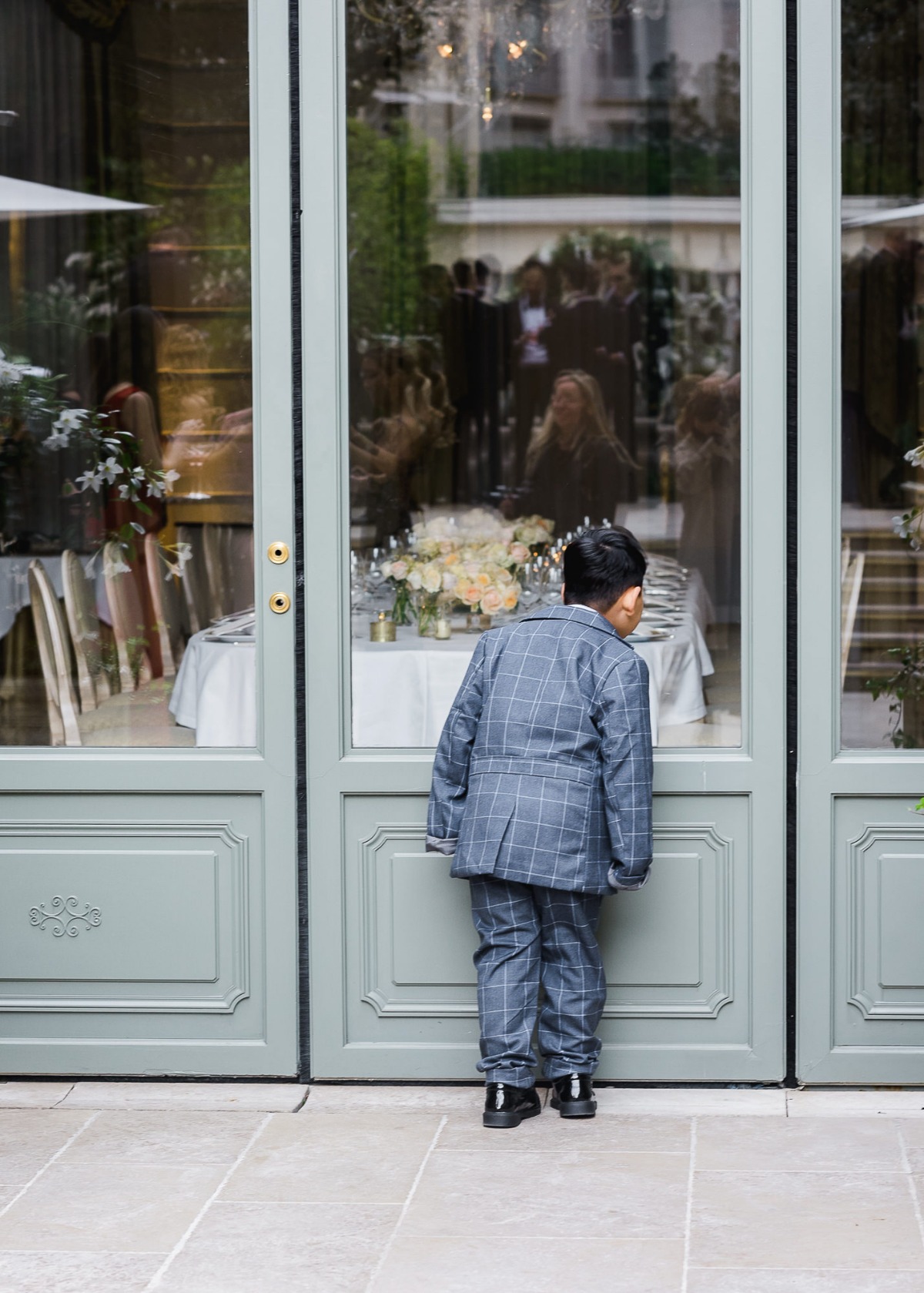 Boy in a suit looks through glass door at a wedding party