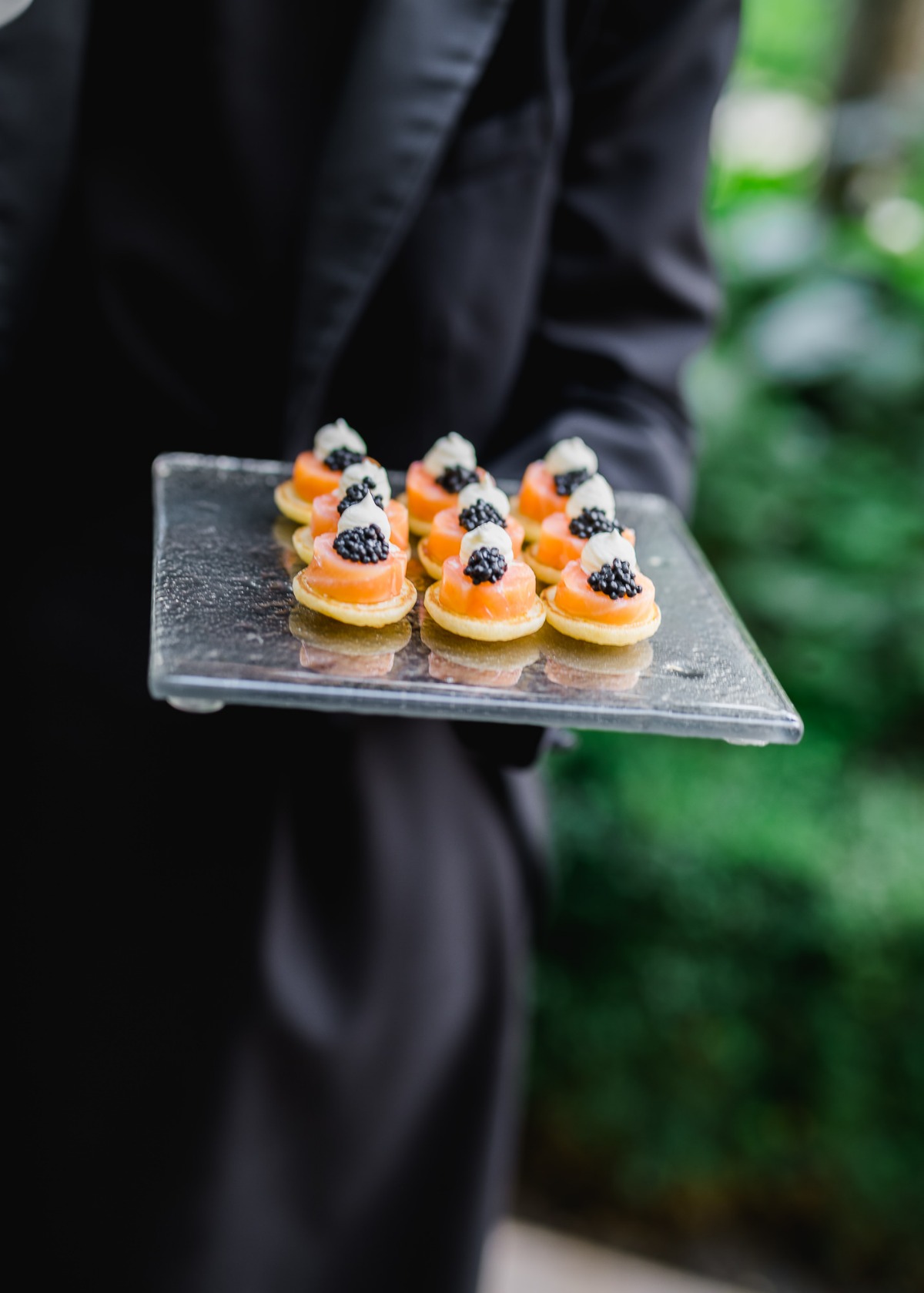 A server presents a tray of elegant appetizers with salmon and caviar