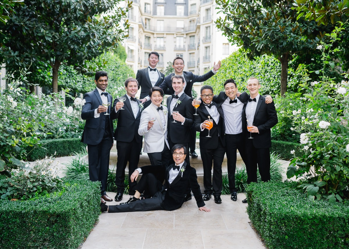Groomsmen in tuxedos celebrate with drinks in a garden setting