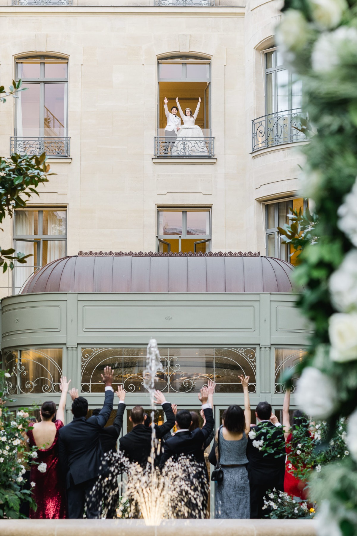 Bride and groom wave to cheering guests from a balcony window
