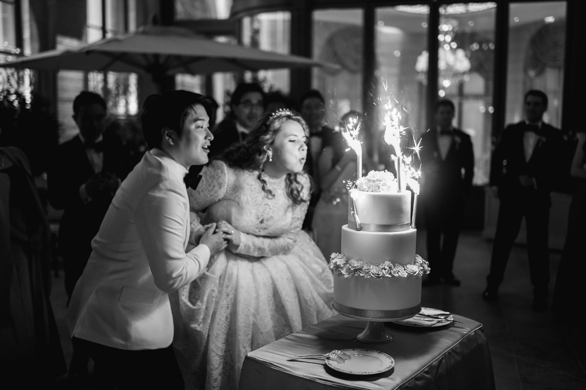 Couple blowing sparklers on wedding cake with joy, black and white