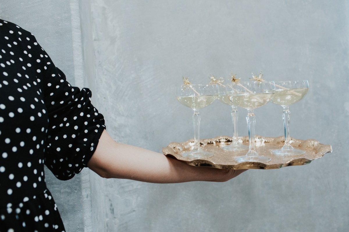 Woman holding champagne glasses on a gold tray for a celebration