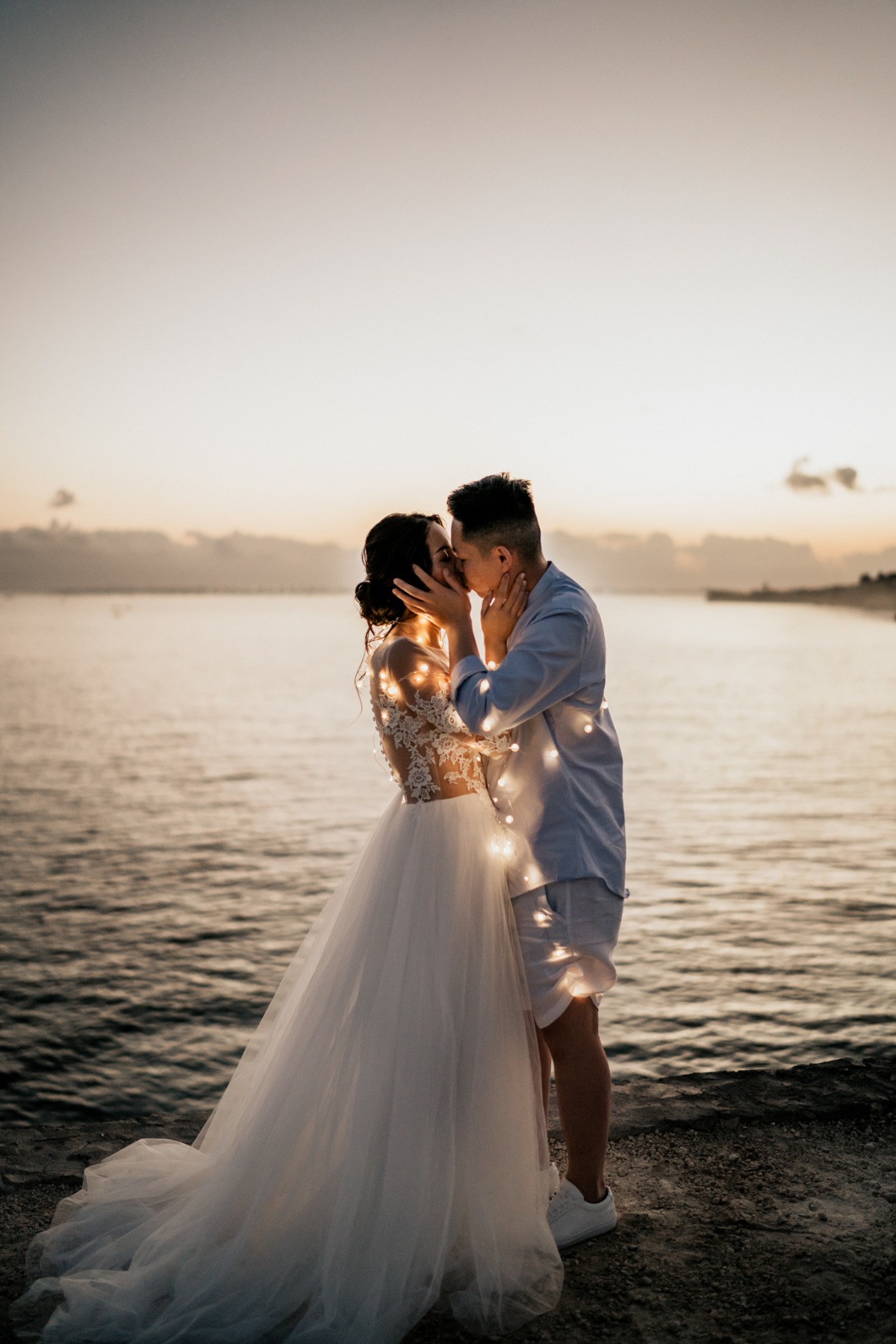 Couple kissing at sunset with string lights, wedding photo
