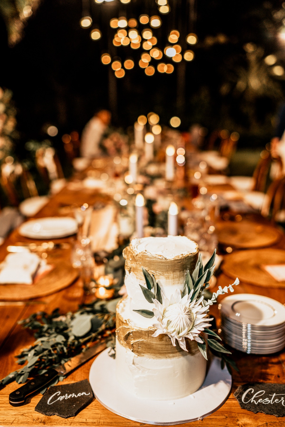 White and gold wedding cake on candlelit reception table