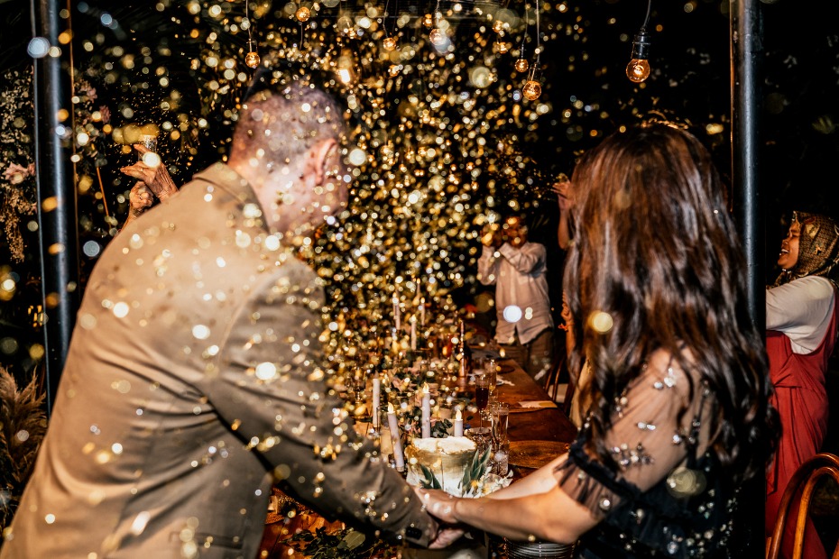 Joyful couple cutting wedding cake under gold confetti