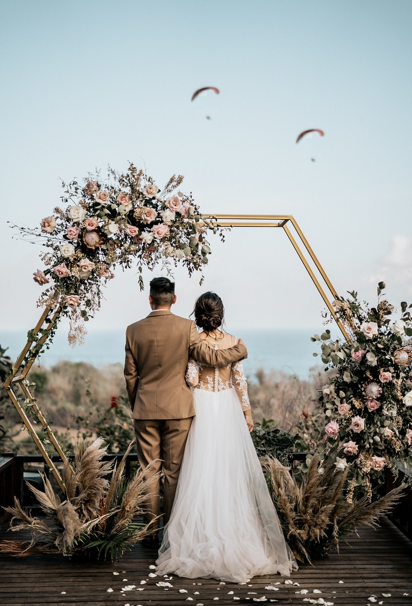 Bride and groom under floral arch enjoy ocean view