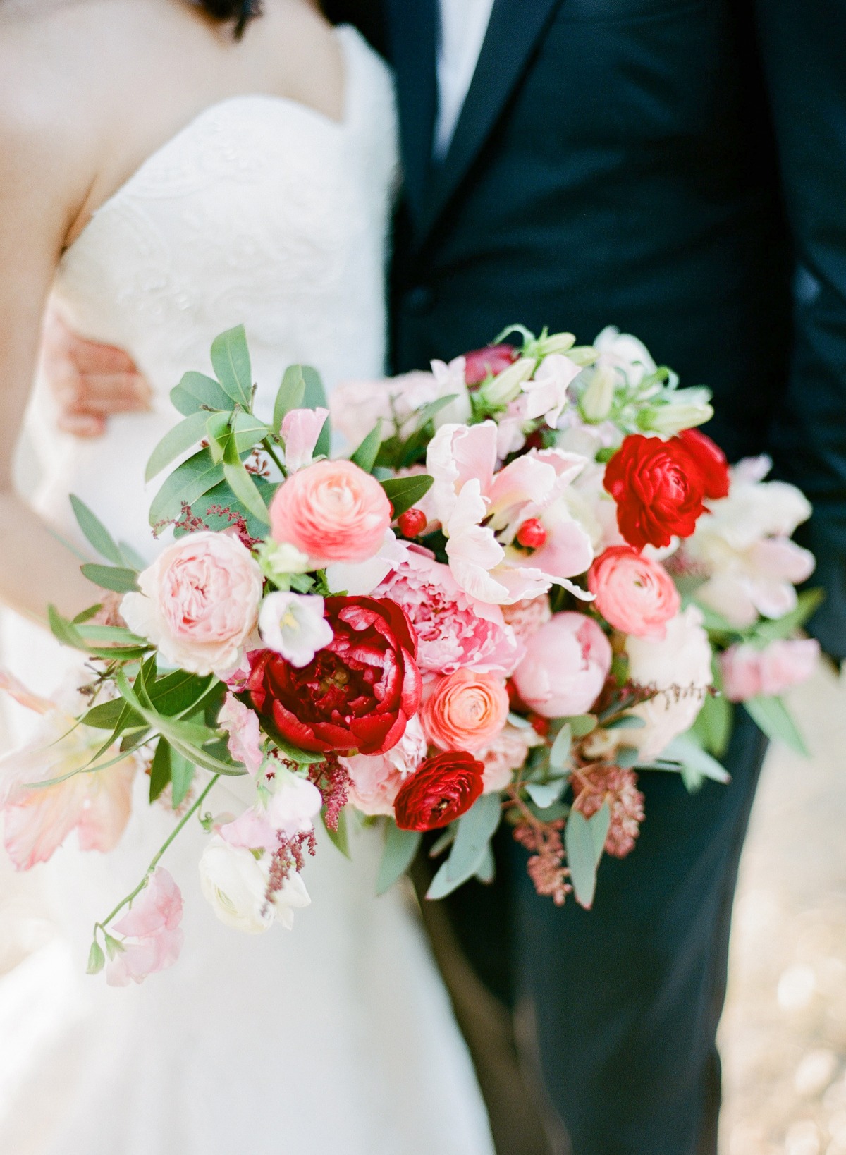 Bride holding a colorful wedding bouquet with red and pink flowers