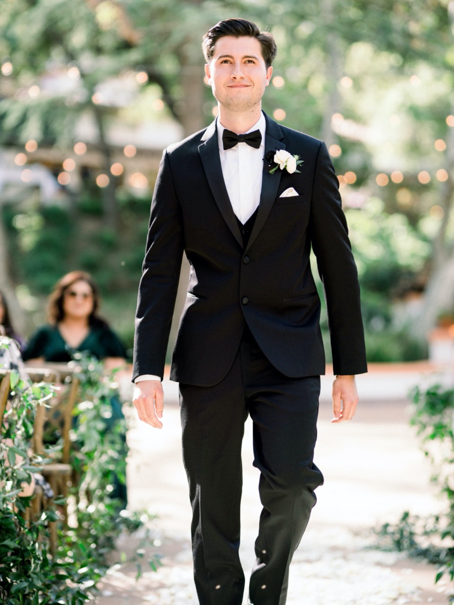 Groom in tuxedo walking down wedding aisle outdoors