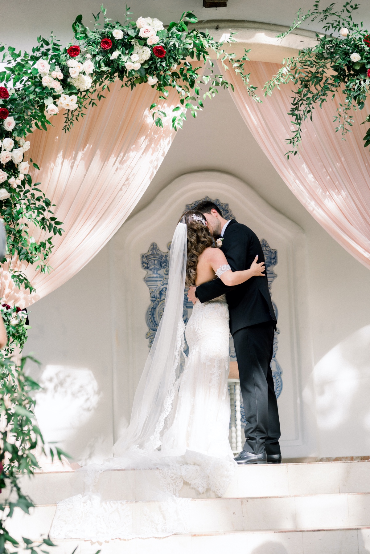 Bride and groom kissing under a floral wedding arch