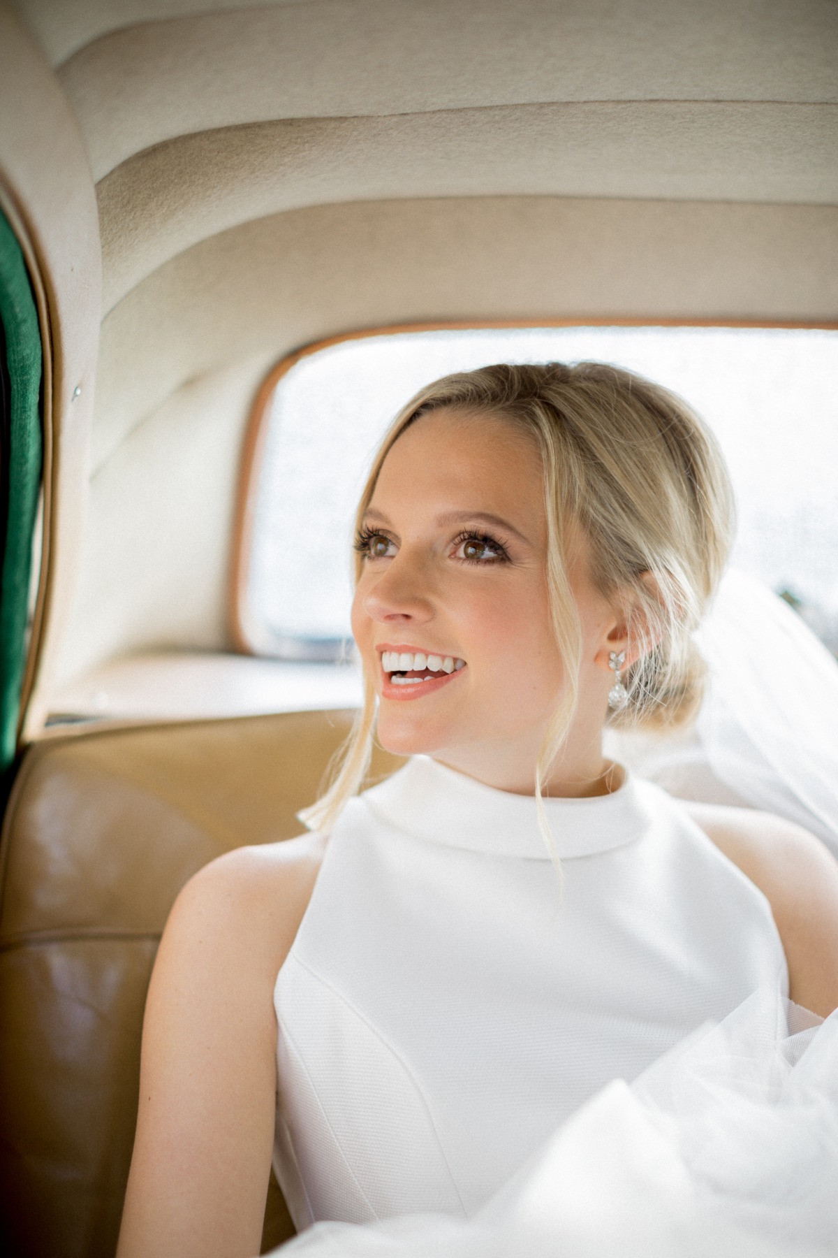 Blonde bride smiles inside vintage car on wedding day