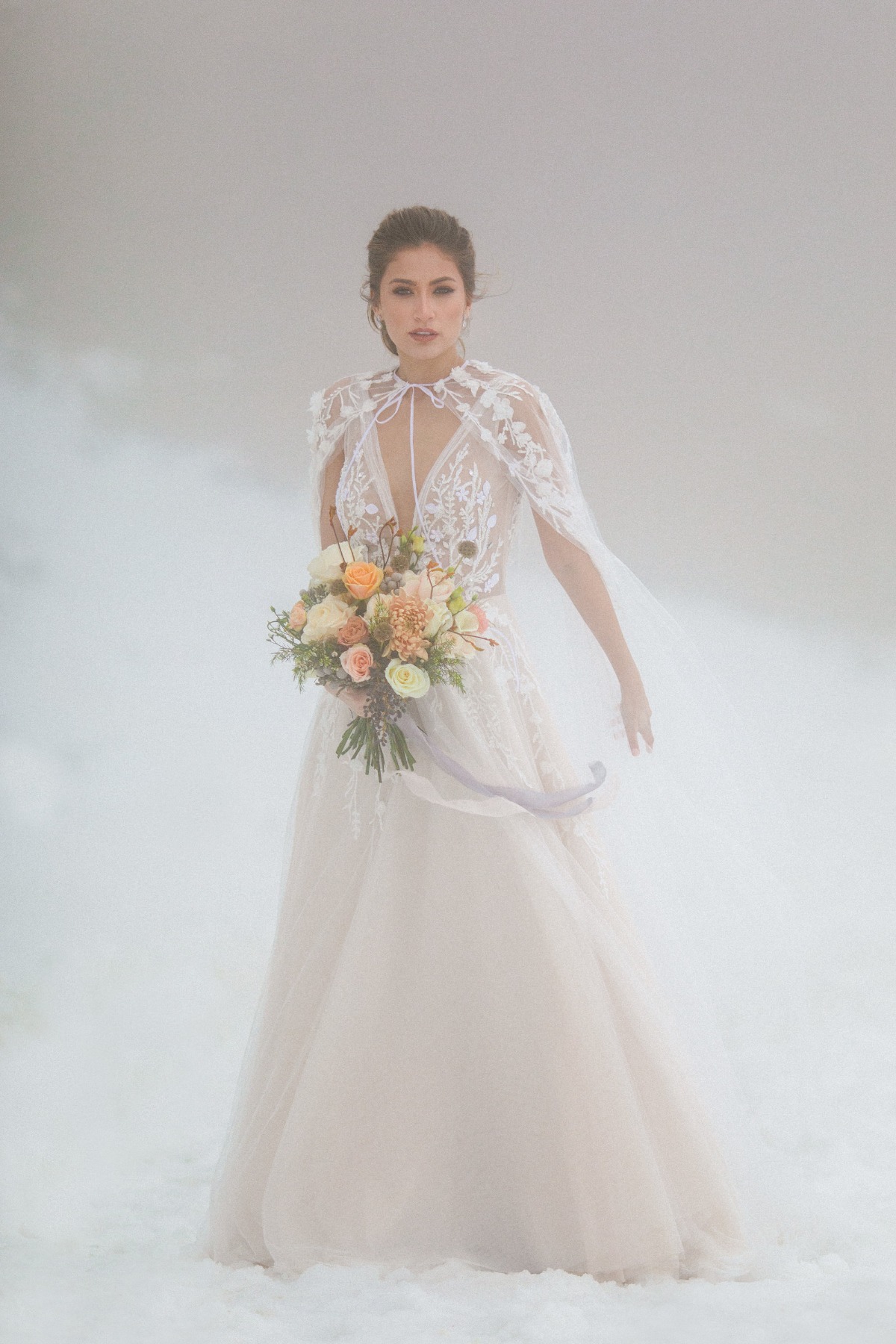 Bride in ethereal gown holding bouquet in dreamy fog