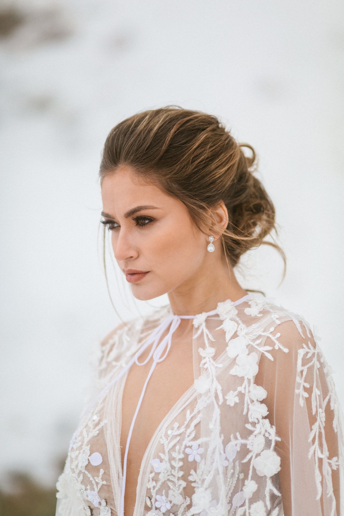 Elegant bride in a floral lace dress looking away in the snow