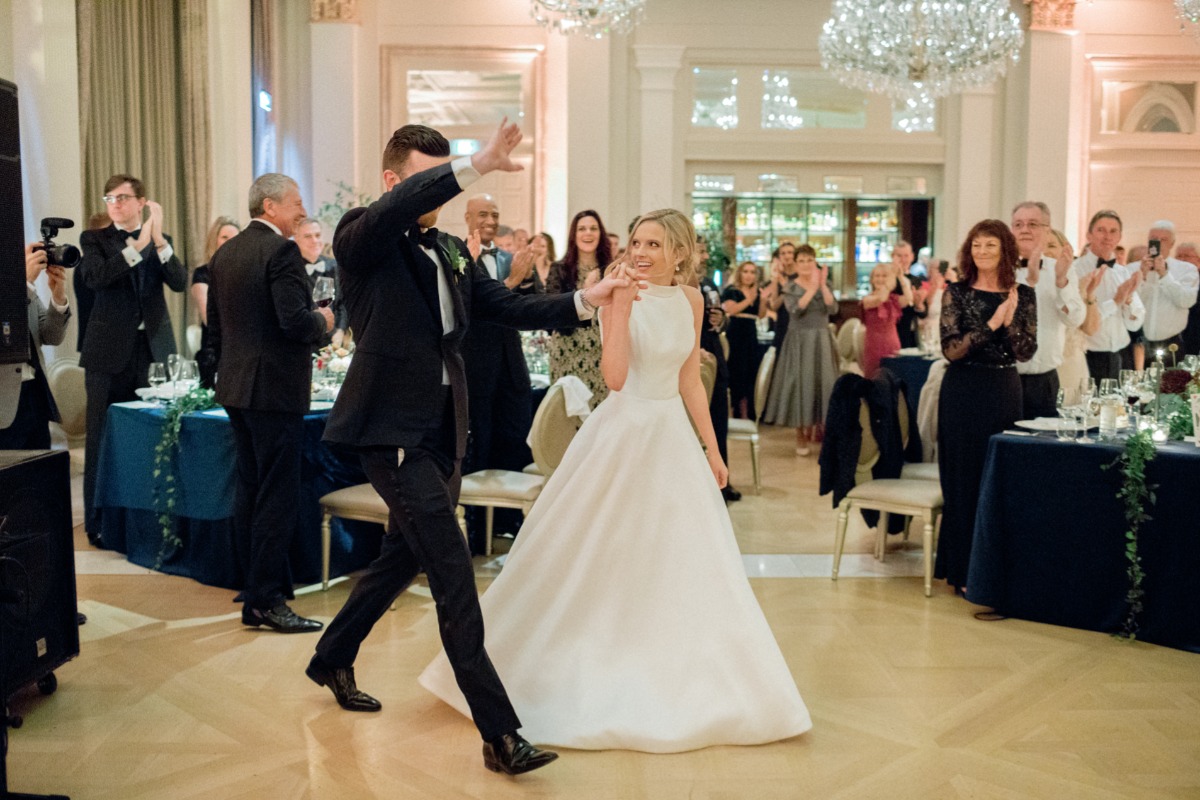 Newlyweds dancing at a wedding reception with guests applauding joyfully