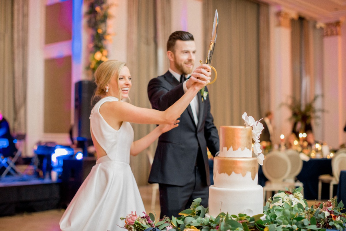 Bride and groom cut cake with sword at wedding reception