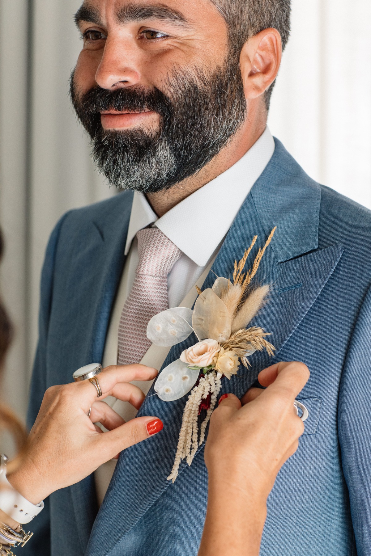 Groom getting a boutonniere pinned on his jacket at wedding