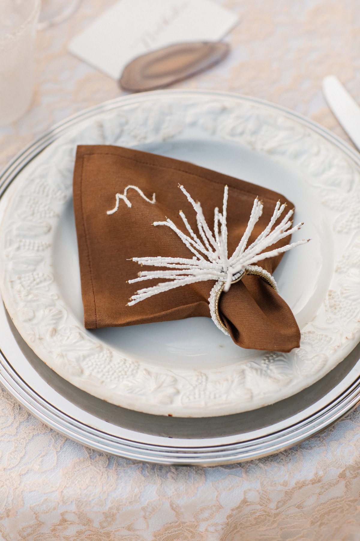 Elegant table setting with a brown napkin and white beaded ring