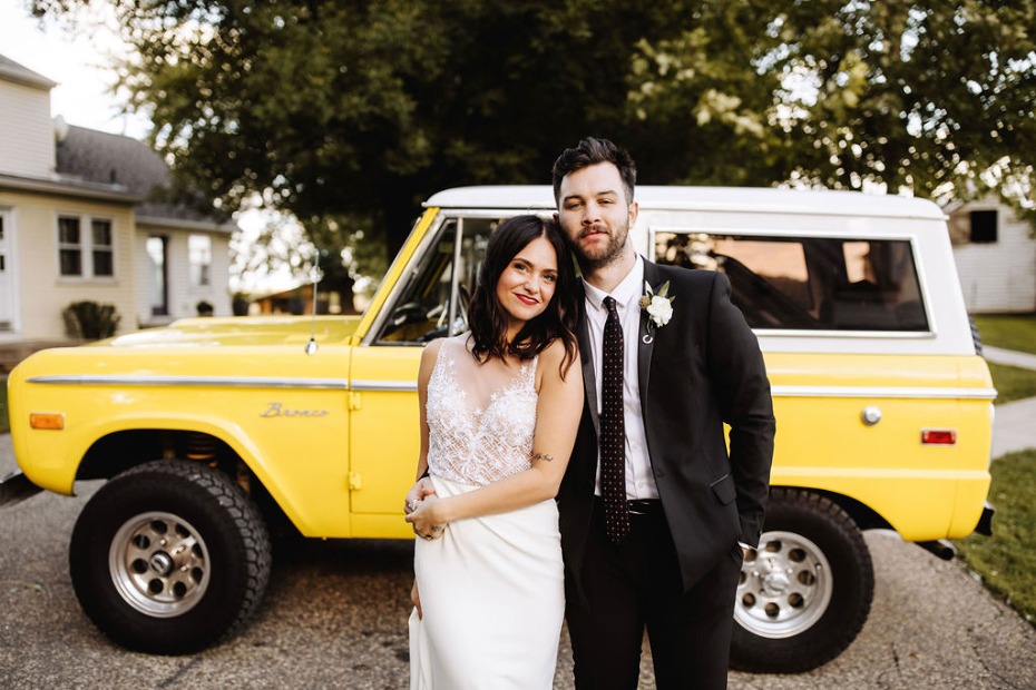 Newlyweds pose in front of a yellow vintage Bronco on their wedding day