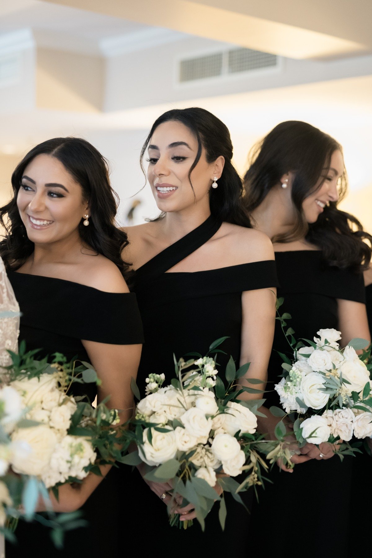 black bridesmaid dresses with white bouquets and pearl earrings