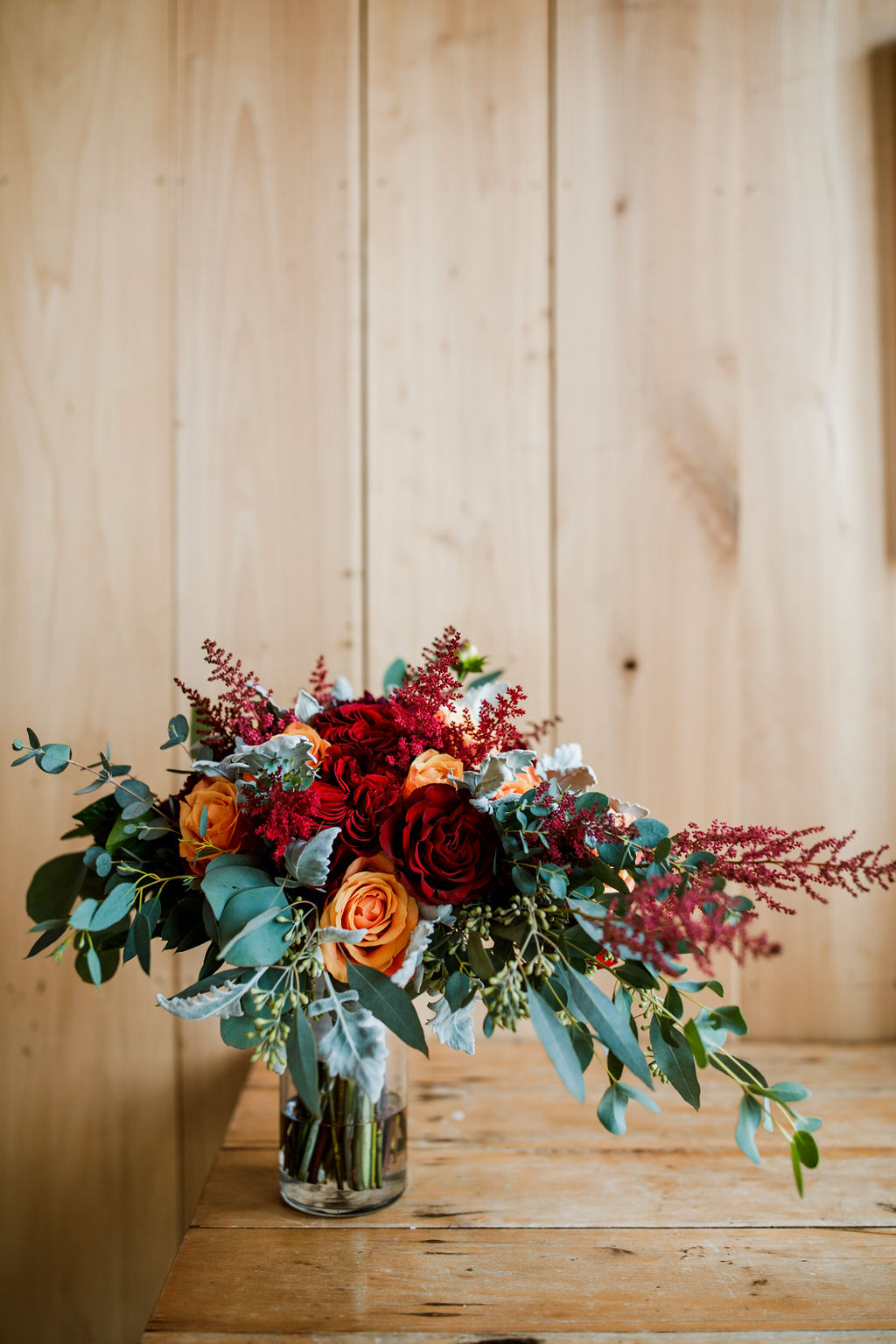 Elegant red and orange roses in glass vase on wood table