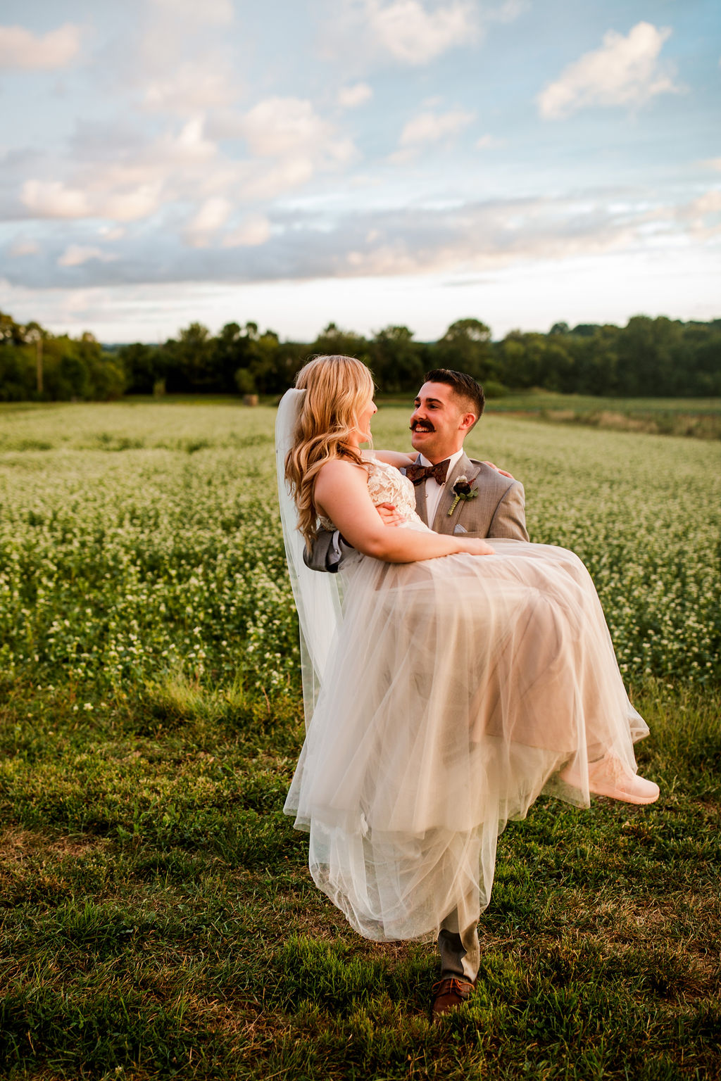 Groom carries his bride in a beautiful field setting