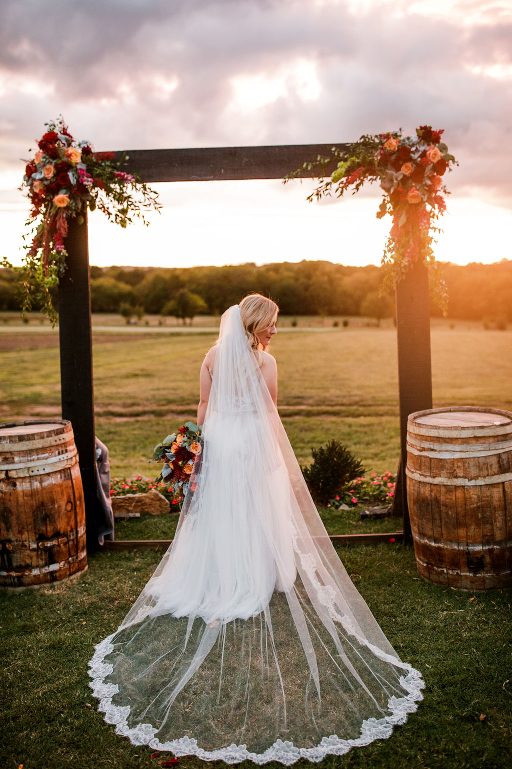 Bride in veil at rustic wedding ceremony archway sunset