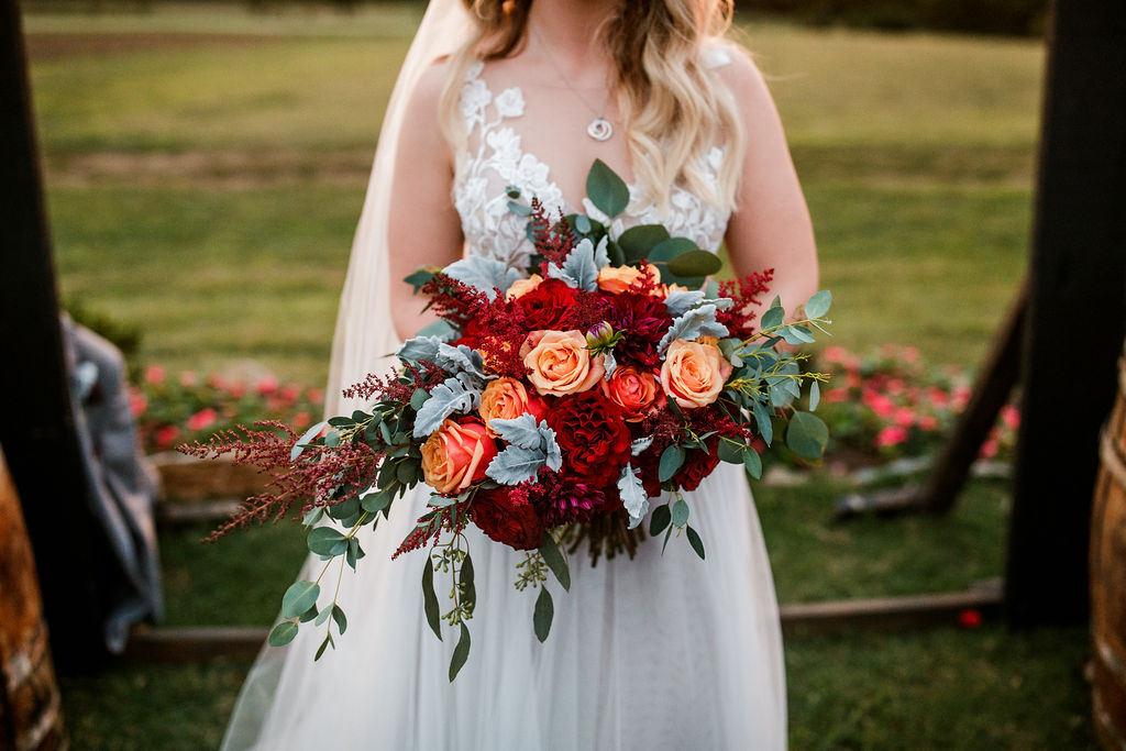 Bride in white dress holds orange and red wedding bouquet