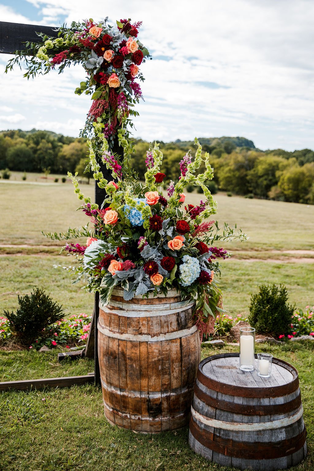 outdoor wedding ceremony set up with lush floral arrangements on barrels