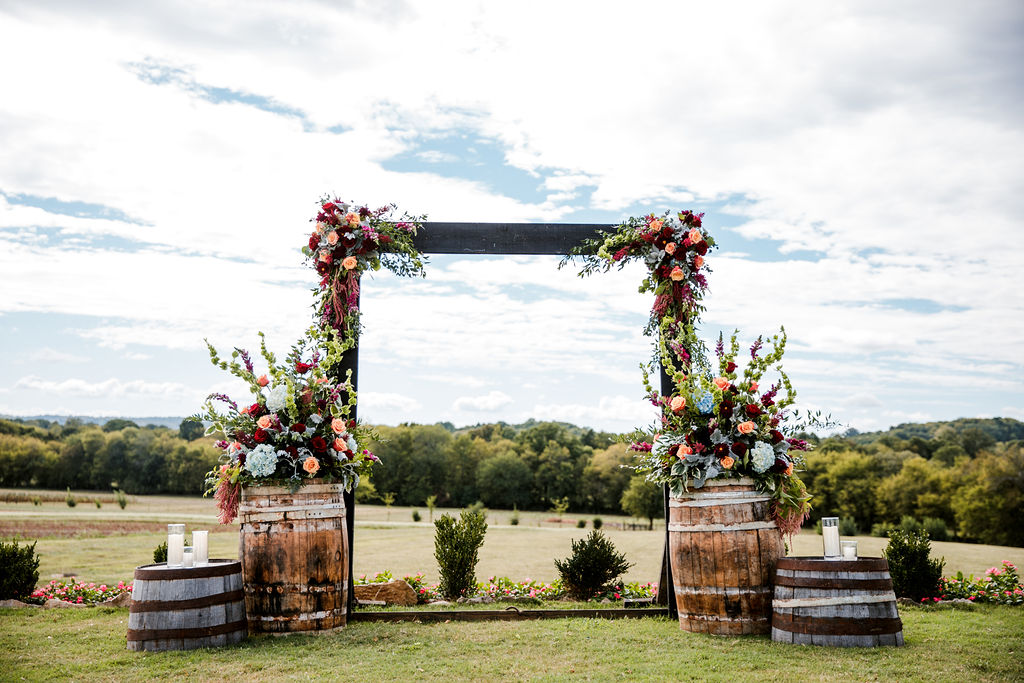 outdoor wedding ceremony set up with lush floral arrangements on barrels