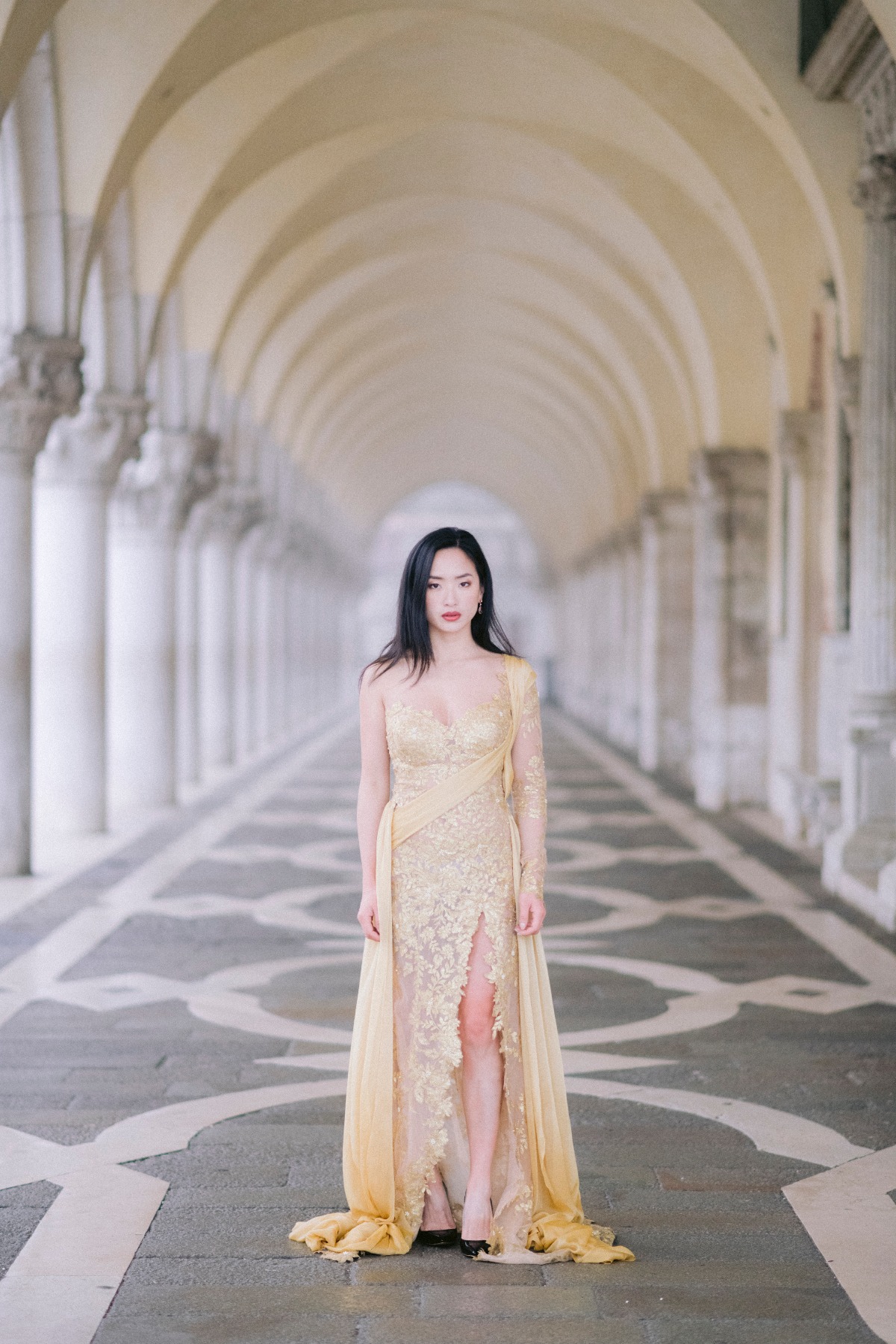 Elegant woman in gold dress walking in grand arched corridor