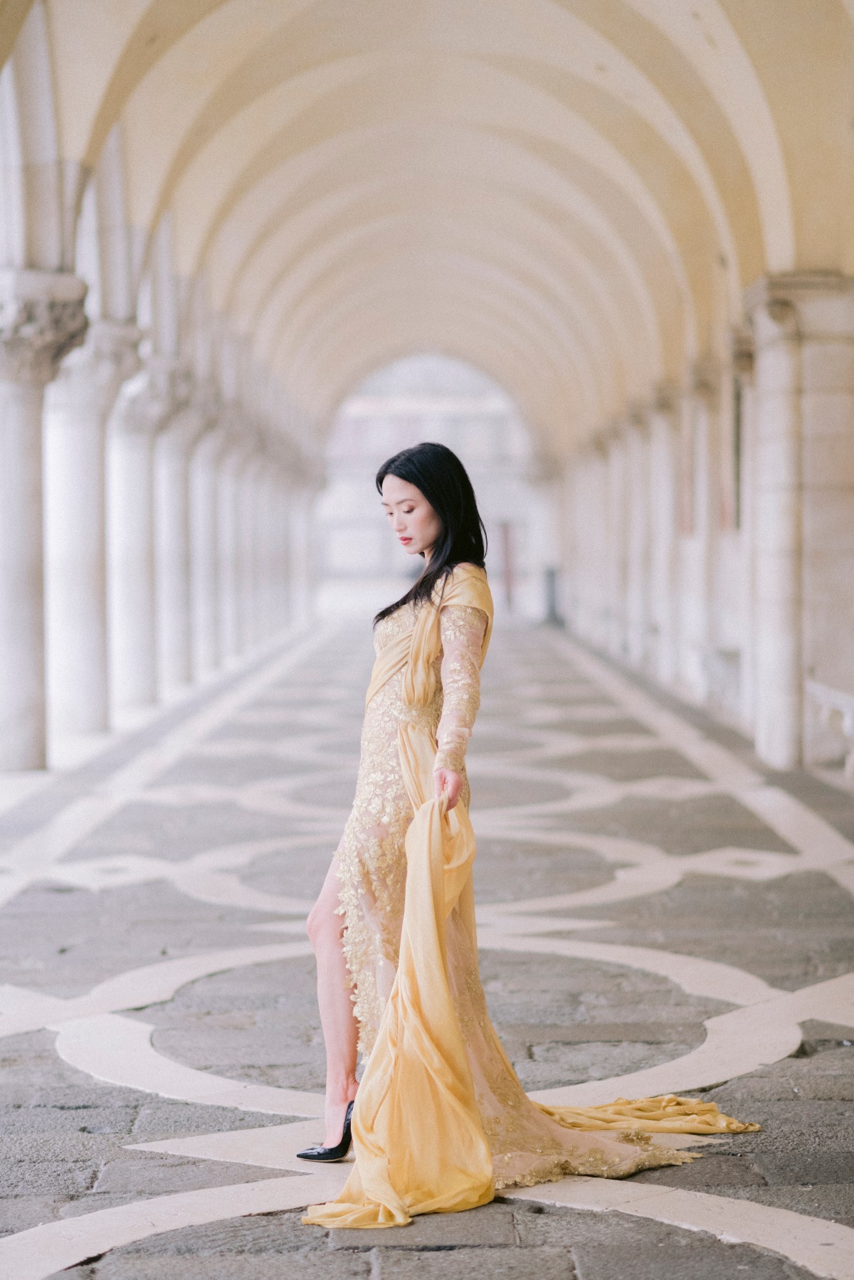 Elegant woman in golden dress walks under arched corridor