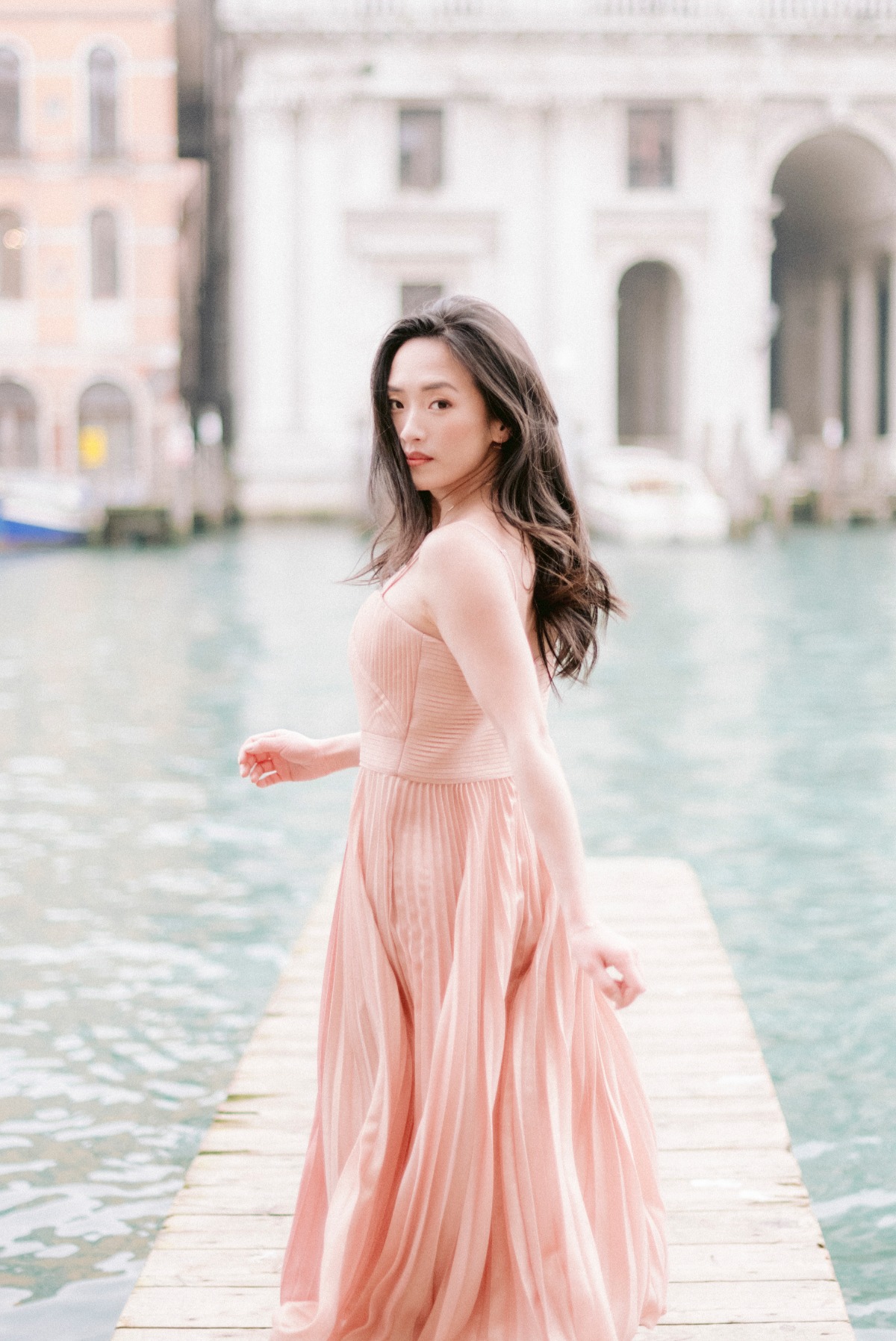 Woman in a pink dress on a wooden pier, Venice backdrop