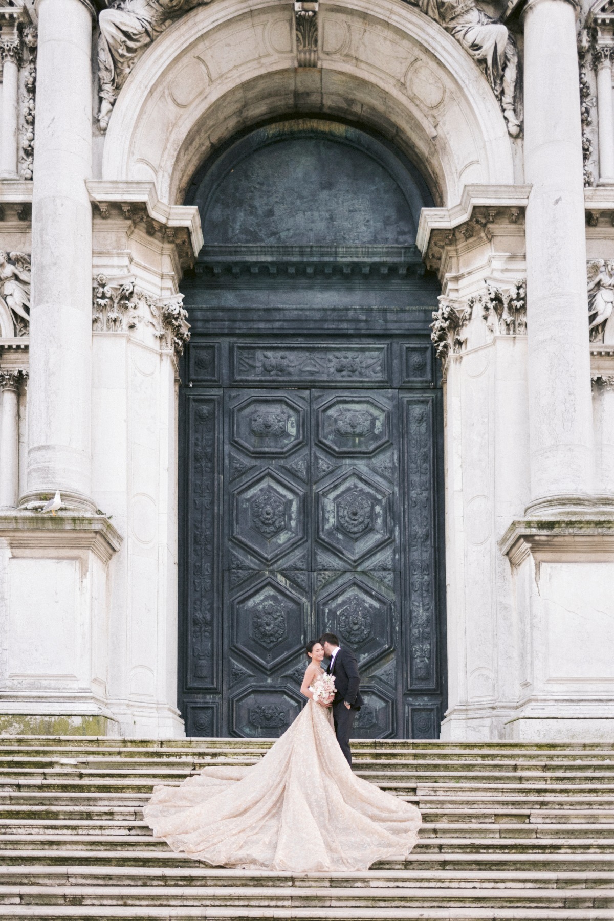 Bride and groom embrace at grand church entrance, romantic wedding photo