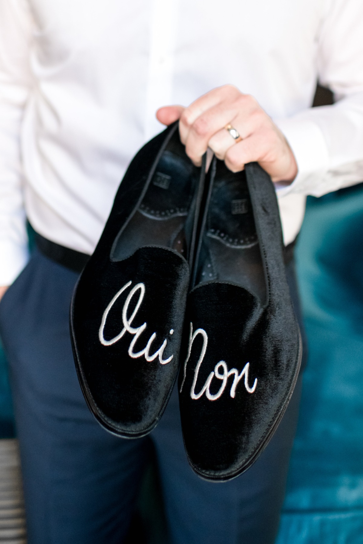 Groom holding black velvet shoes with Oui Non embroidered on them