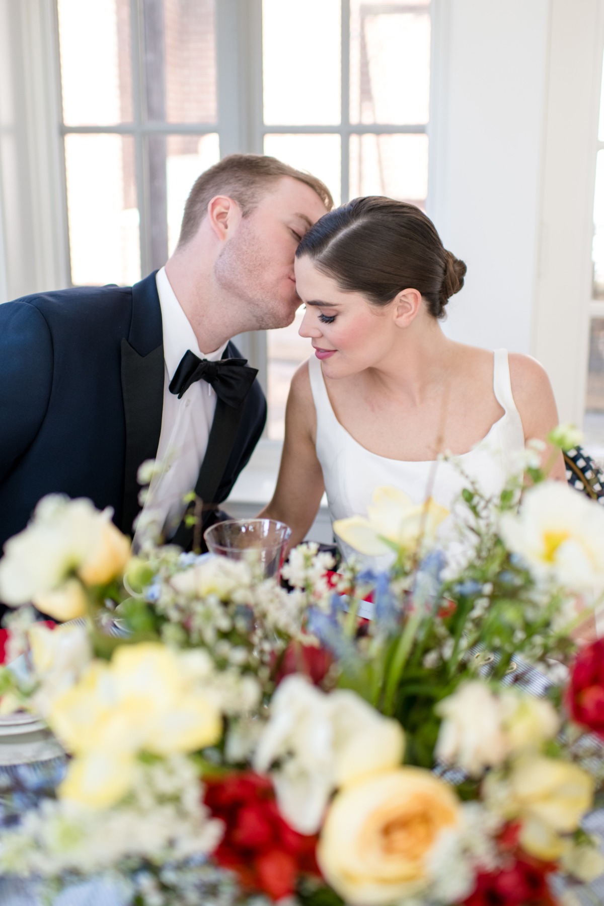 Happy couple at a wedding, groom kisses bride, floral table