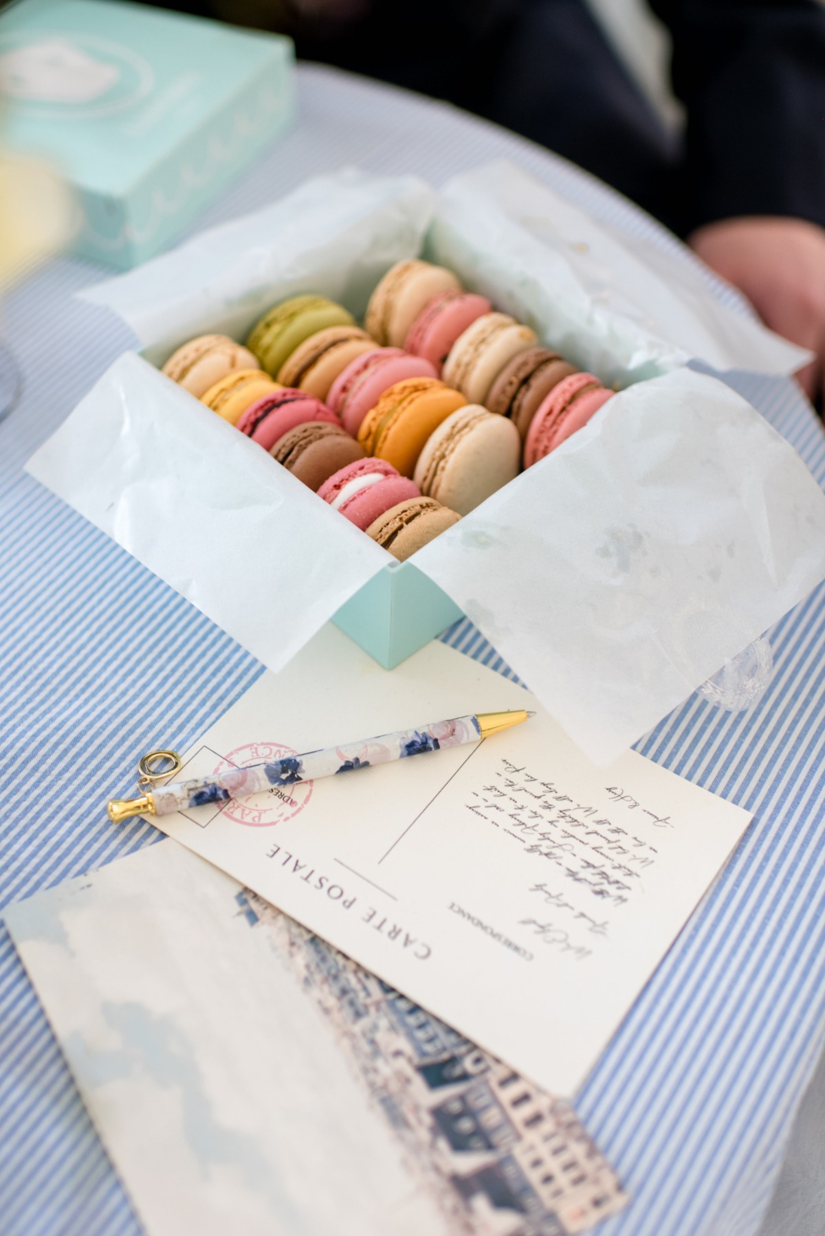Box of colorful macarons with postcards and a floral pen