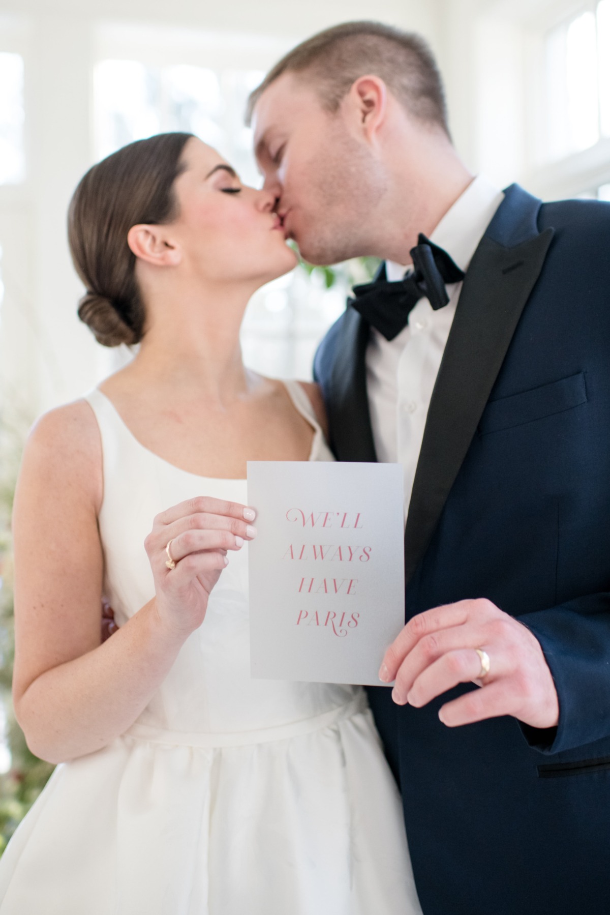 Bride and groom kiss holding We'll Always Have Paris card