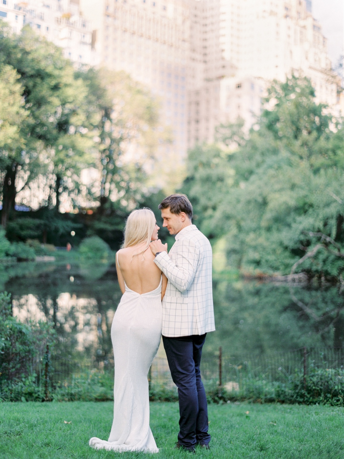 A couple gazing lovingly in a park near a lake, in a dress