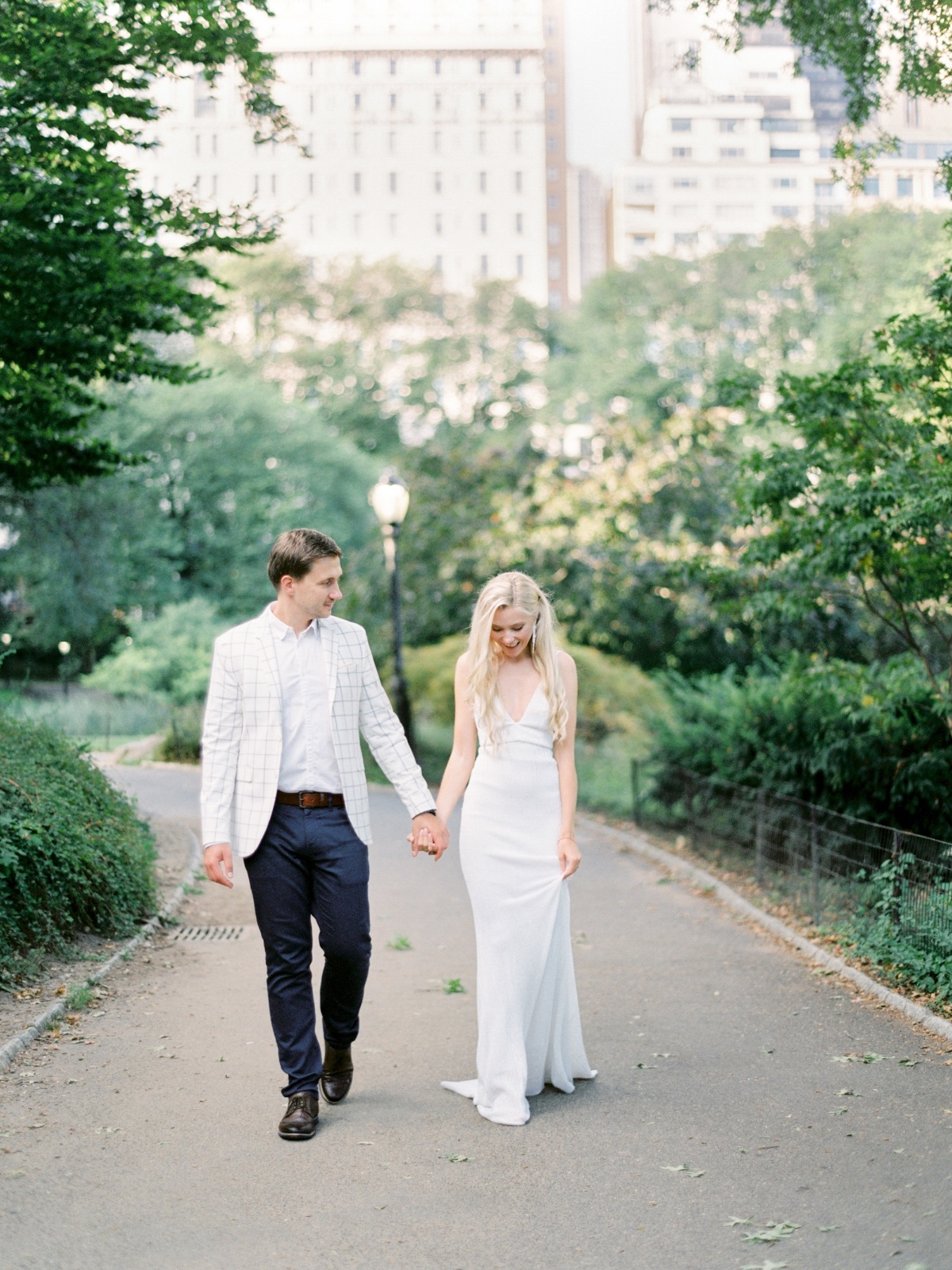 Elegant couple holding hands walking in a park with city in the background