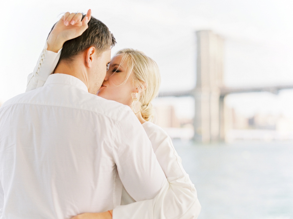 Couple kissing in front of Brooklyn Bridge with blurred background